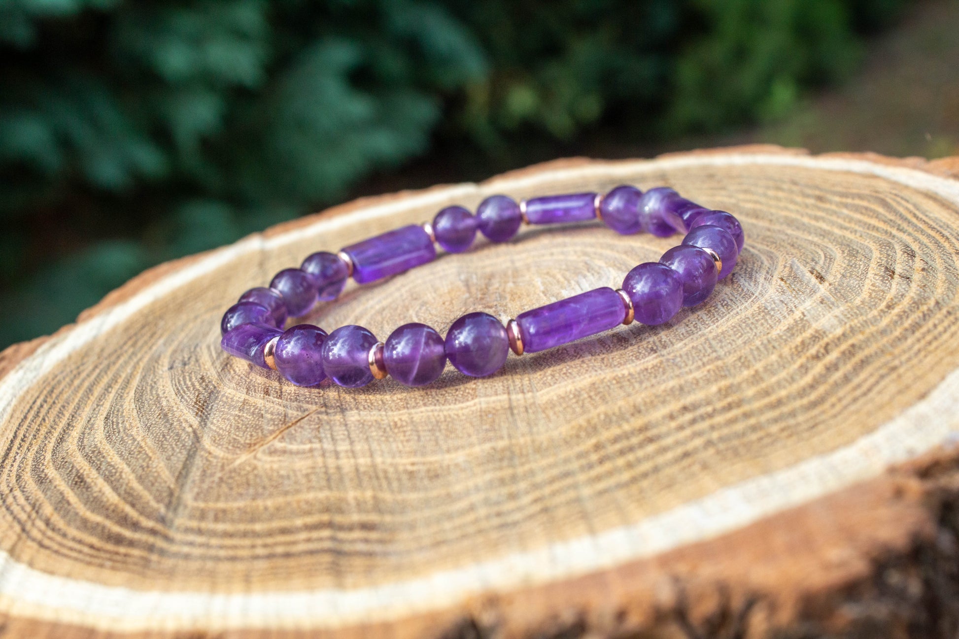 kézzel készült ametiszt karkötő ametiszt gyöngy és hasábok felhasználásával, rosegold hematit korongokkal, fa felületen fotózva, a Lila Harmónia kollekcióbóll