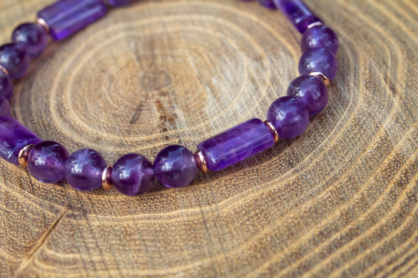 kézzel készült ametiszt karkötő ametiszt gyöngy és hasábok felhasználásával, rosegold hematit korongokkal, fa felületen fotózva, a Lila Harmónia kollekcióbóll