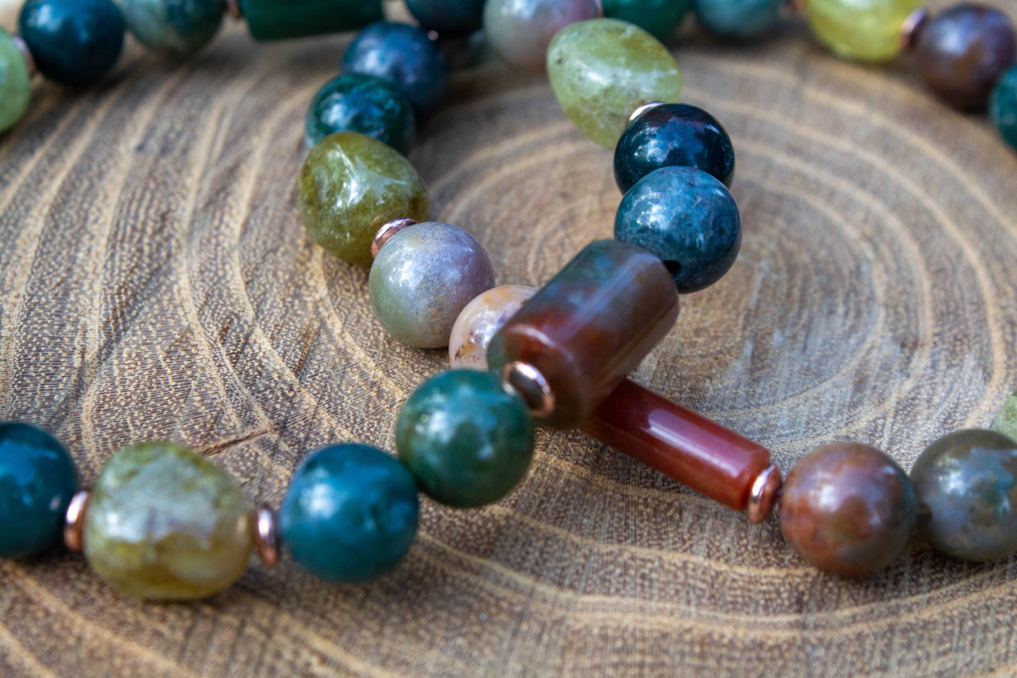 egyedi női karkötő indiai achát és gránát grossulat ásványokkal, indiai achát hasábbal, valamint rosegold hematatit köztessel, természtes fa háttérrel