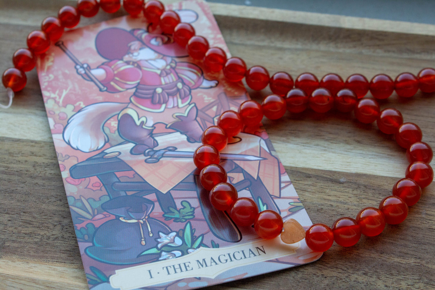 karneol ásványkarkötő, teremtő tűz energiával, spirituális ékszer, a háttérben mágus tarot kártyával